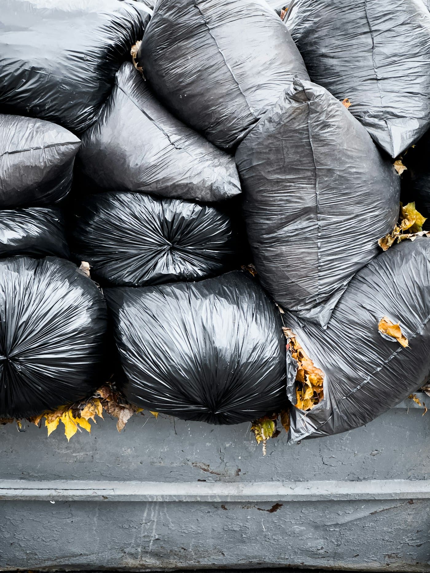 Stack of black commercial waste bags beside a dumpster